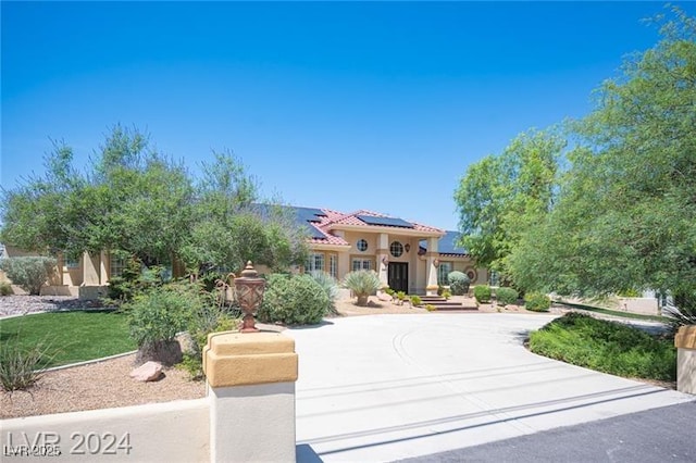 mediterranean / spanish-style house featuring stucco siding, a tile roof, driveway, and solar panels