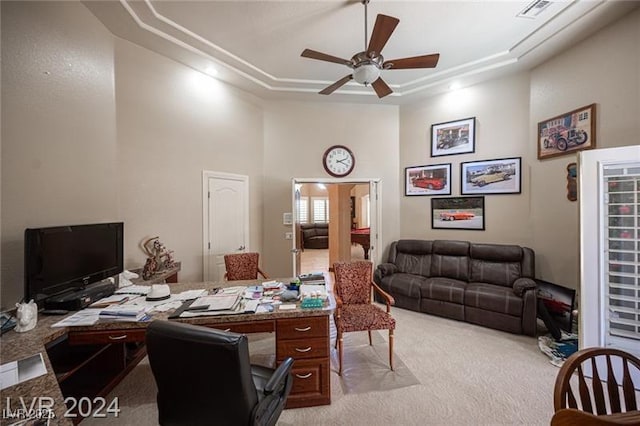 office space with a towering ceiling, ceiling fan, a raised ceiling, and light colored carpet