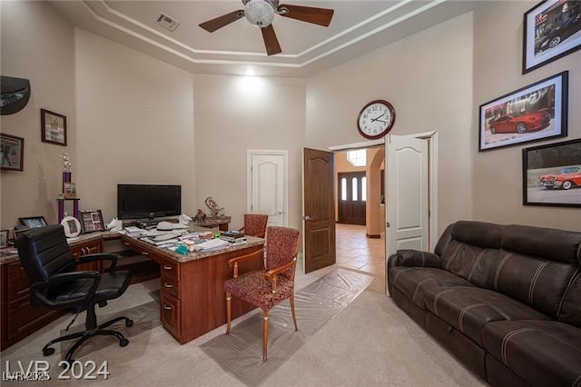 home office featuring ceiling fan, light carpet, a high ceiling, visible vents, and a tray ceiling