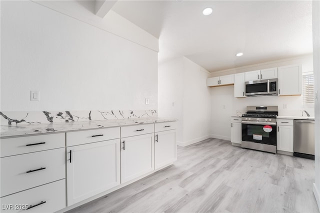 kitchen with stainless steel appliances, white cabinetry, light wood-style flooring, and light stone countertops