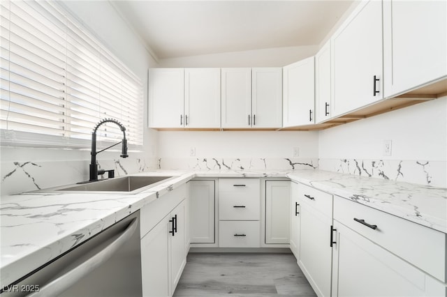 kitchen featuring light stone counters, white cabinetry, a sink, and stainless steel dishwasher