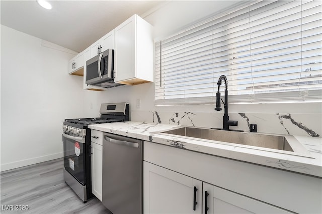 kitchen with stainless steel appliances, white cabinets, a sink, light stone countertops, and baseboards