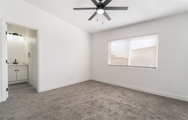 unfurnished bedroom featuring light colored carpet, a sink, a ceiling fan, baseboards, and ensuite bath