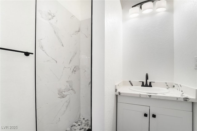 full bath with a textured wall, a marble finish shower, and vanity