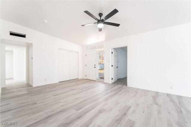 empty room featuring lofted ceiling, light wood-style flooring, visible vents, baseboards, and a ceiling fan