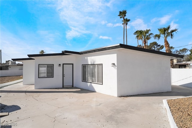 rear view of house with fence, a patio, and stucco siding