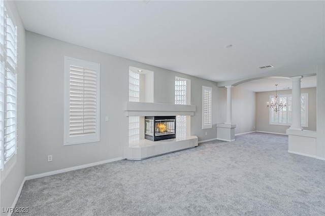 unfurnished living room featuring a chandelier, carpet flooring, visible vents, a glass covered fireplace, and ornate columns