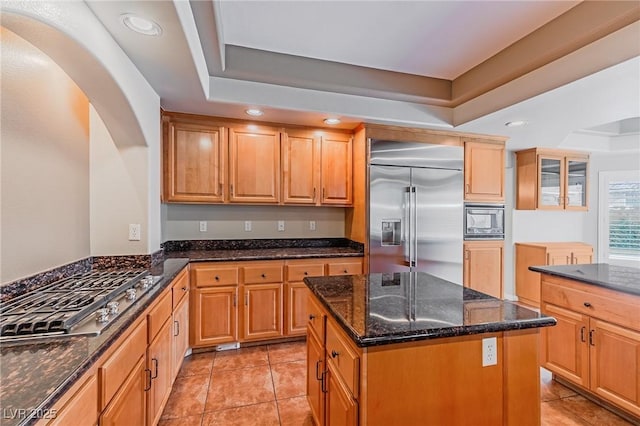 kitchen with dark stone counters, a raised ceiling, recessed lighting, and built in appliances