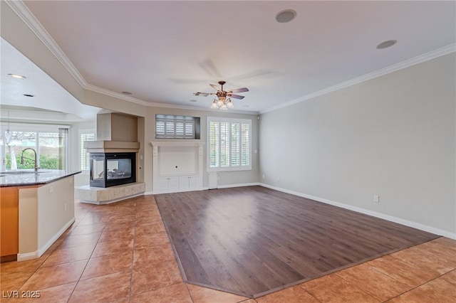 unfurnished living room featuring light tile patterned floors, baseboards, crown molding, a sink, and a multi sided fireplace