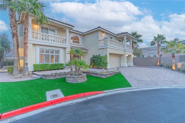 mediterranean / spanish-style home with a balcony, a tile roof, decorative driveway, a front yard, and stucco siding