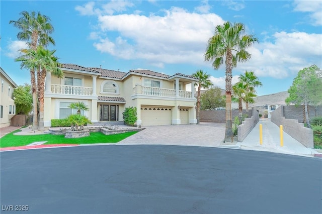 mediterranean / spanish-style house with decorative driveway, stucco siding, an attached garage, fence, and a balcony