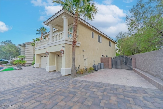 view of property exterior featuring an attached garage, cooling unit, decorative driveway, a gate, and stucco siding