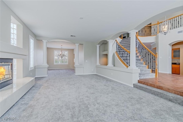 unfurnished living room featuring decorative columns, visible vents, an inviting chandelier, stairs, and carpet floors