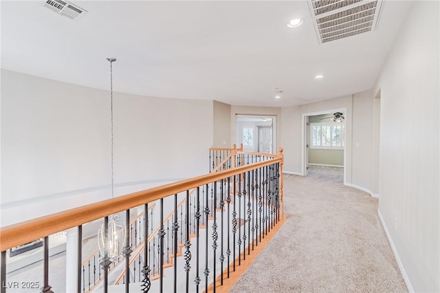 hall featuring carpet, visible vents, baseboards, and an upstairs landing