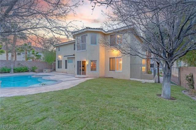 back of house at dusk featuring a fenced in pool, a yard, a patio, stucco siding, and a fenced backyard