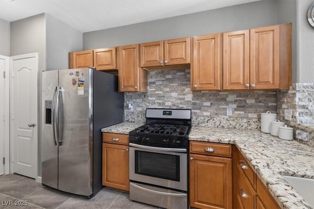 kitchen with stainless steel appliances, light tile patterned flooring, decorative backsplash, and light stone countertops