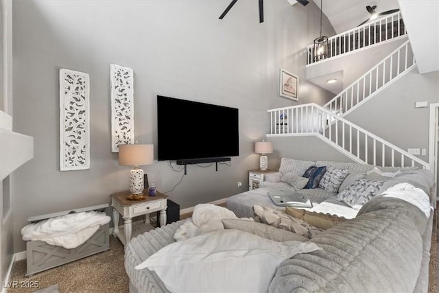 carpeted living room with stairs, ceiling fan, a high ceiling, and baseboards