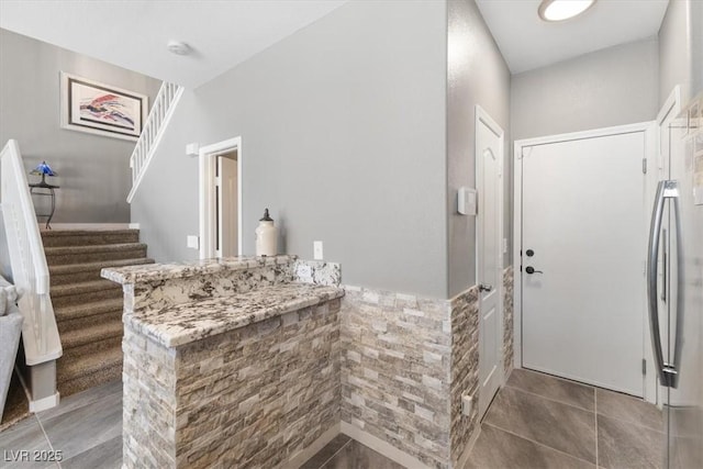 kitchen featuring tile patterned floors, a wainscoted wall, stainless steel refrigerator, and light stone countertops