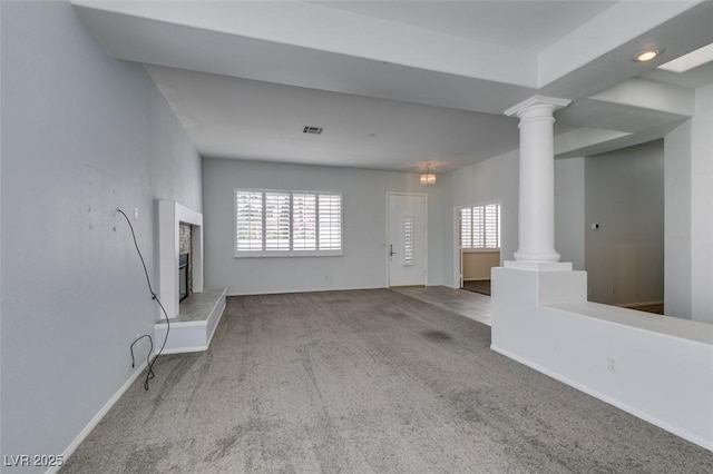 unfurnished living room featuring a wealth of natural light, carpet flooring, visible vents, and ornate columns