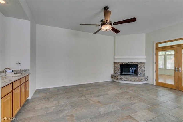 unfurnished living room featuring french doors, a ceiling fan, a glass covered fireplace, a sink, and baseboards