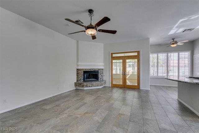 unfurnished living room featuring a ceiling fan, visible vents, baseboards, french doors, and a glass covered fireplace