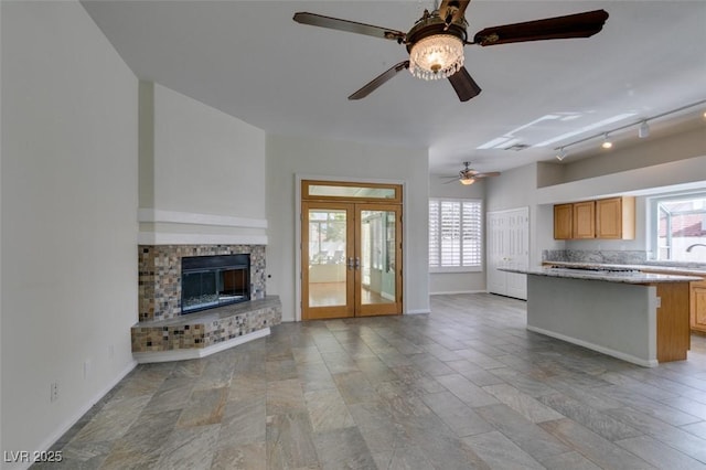 unfurnished living room featuring baseboards, a ceiling fan, rail lighting, french doors, and a fireplace