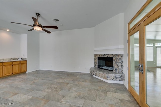 unfurnished living room with a fireplace, a sink, visible vents, and baseboards