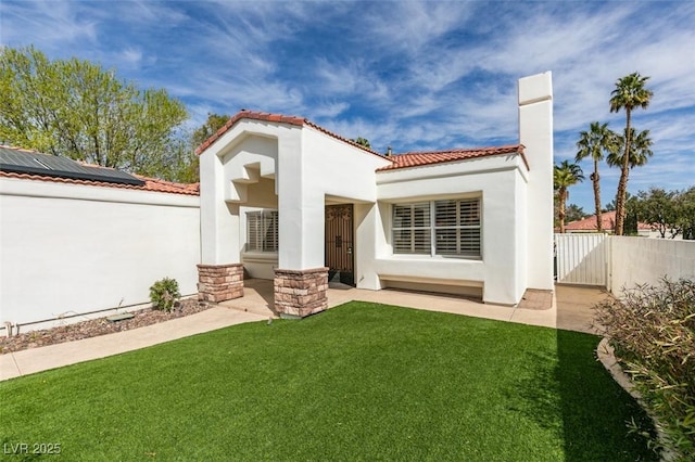 back of house with a tiled roof, a lawn, fence, and stucco siding