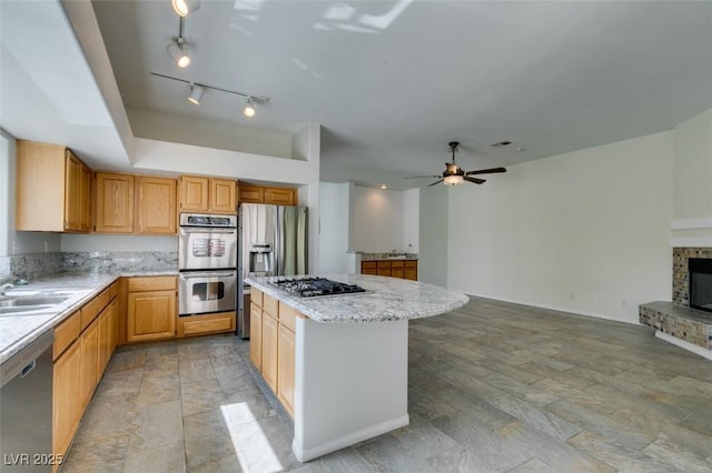 kitchen with ceiling fan, a fireplace, a kitchen island, a sink, and appliances with stainless steel finishes