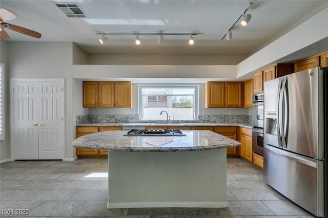 kitchen with stainless steel appliances, a kitchen island, visible vents, light stone countertops, and brown cabinetry