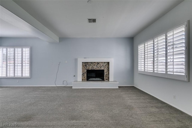 unfurnished living room with baseboards, visible vents, a fireplace with raised hearth, carpet floors, and beam ceiling