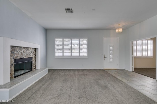 unfurnished living room with carpet floors, visible vents, a chandelier, and a glass covered fireplace