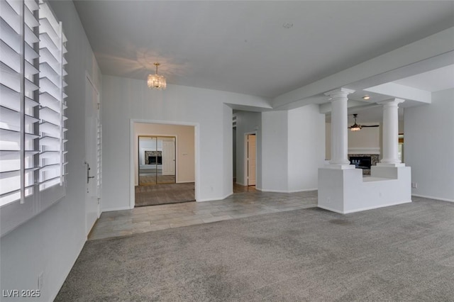 unfurnished living room featuring decorative columns, baseboards, ceiling fan, and carpet flooring