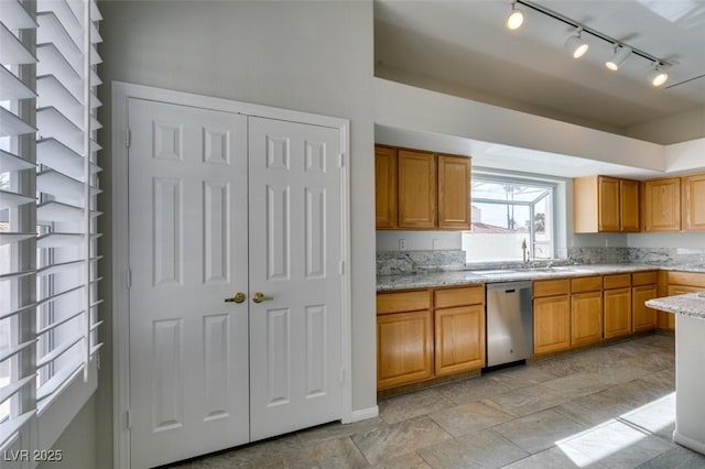 kitchen featuring light stone counters, brown cabinetry, a sink, and stainless steel dishwasher