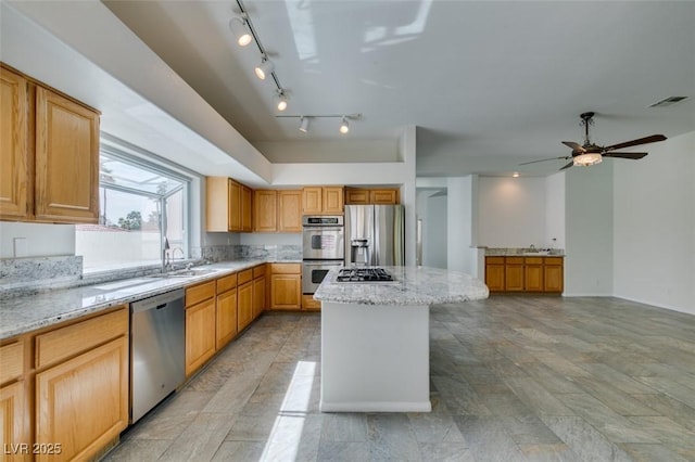 kitchen with light stone counters, a center island, stainless steel appliances, visible vents, and a sink