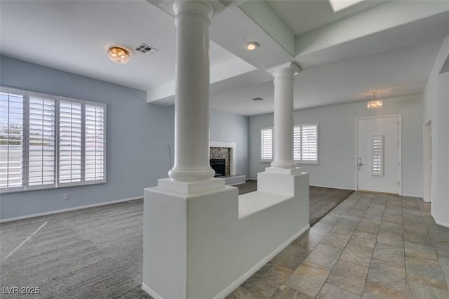 carpeted living area featuring decorative columns, visible vents, and a fireplace with raised hearth