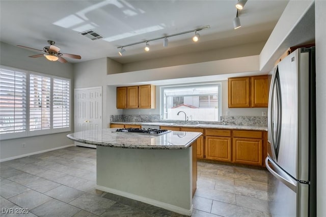 kitchen featuring stainless steel appliances, a sink, visible vents, brown cabinets, and light stone countertops