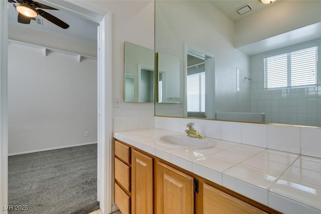 full bath featuring baseboards, visible vents, tiled shower, ceiling fan, and vanity