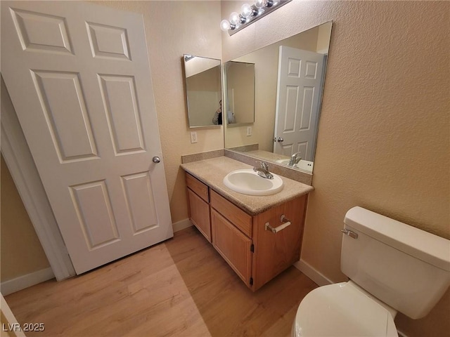 half bathroom featuring baseboards, vanity, toilet, and wood finished floors