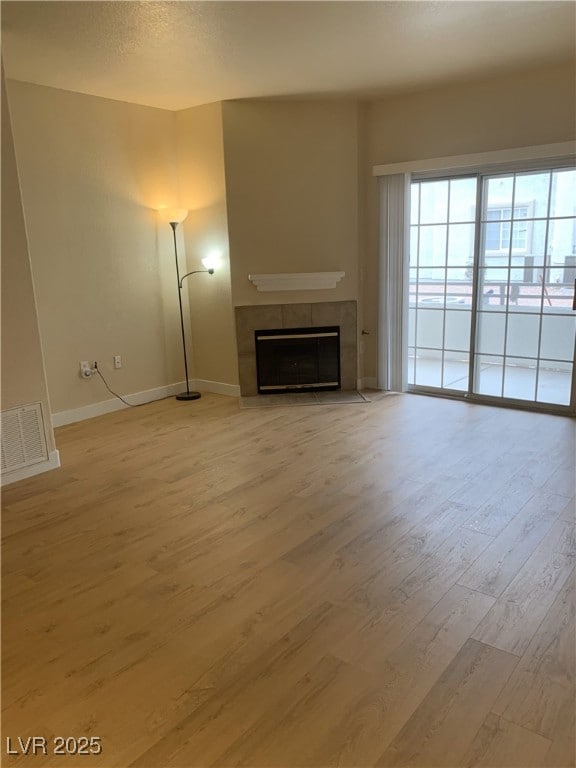 unfurnished living room featuring baseboards, a tiled fireplace, visible vents, and light wood-style floors