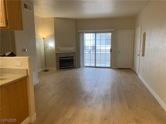 unfurnished living room with a textured ceiling, light wood-type flooring, a fireplace, and visible vents