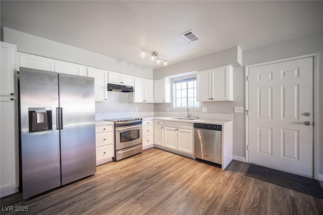 kitchen with under cabinet range hood, a sink, visible vents, light countertops, and appliances with stainless steel finishes