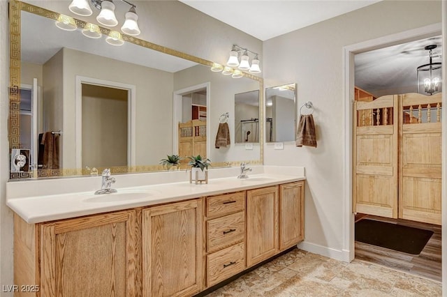 bathroom featuring double vanity, a notable chandelier, baseboards, and a sink