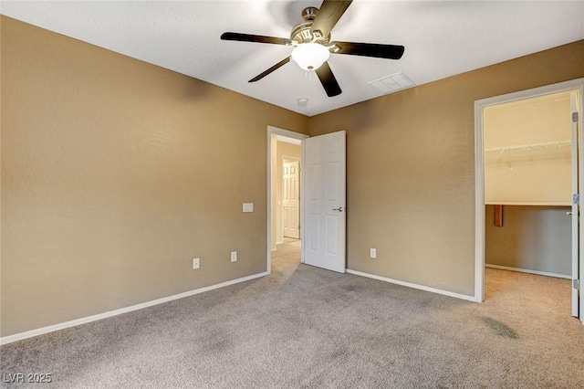 unfurnished bedroom with a walk in closet, baseboards, ceiling fan, and carpet flooring