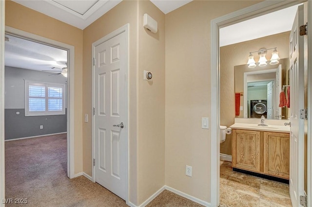 corridor with a sink, baseboards, light carpet, and stacked washing maching and dryer