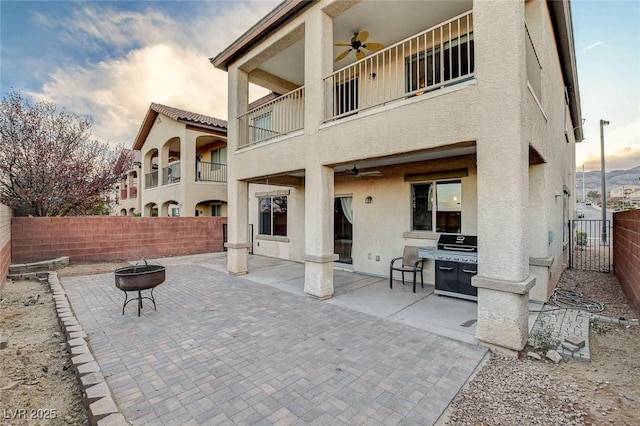 rear view of house featuring stucco siding, a fire pit, ceiling fan, and fence