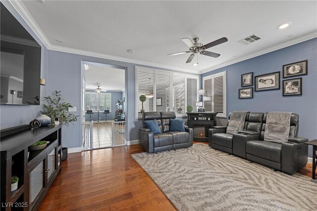 living area with a ceiling fan, visible vents, ornamental molding, and wood finished floors