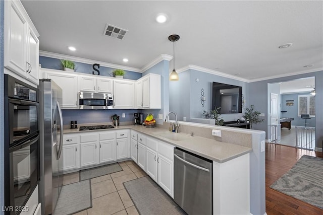 kitchen with stainless steel appliances, a peninsula, a sink, visible vents, and ornamental molding