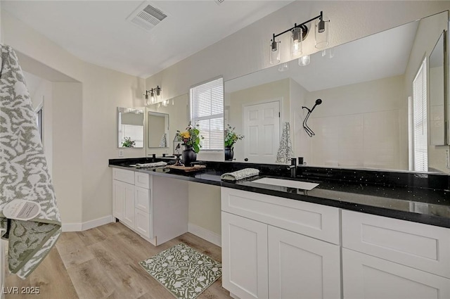 full bath with a sink, wood finished floors, visible vents, a tile shower, and double vanity