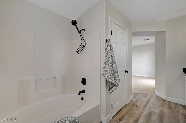 bathroom featuring shower / bath combination, baseboards, visible vents, and wood finished floors